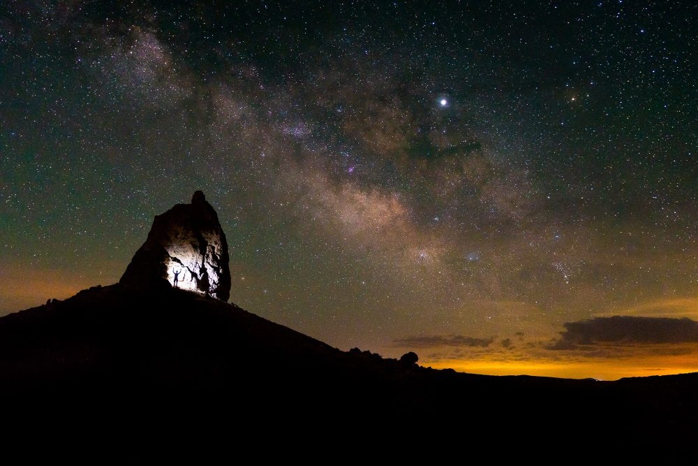 astrophotography long exposure silhouette of person against a rock under the milky way at trona pinnacles shot with sony a7rii and sony 16-35 gm | photo by jake landon schwartz